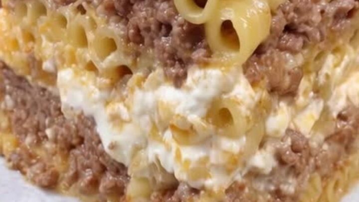 A steaming, golden-brown slice of Greek pastitsio on a white plate with visible layers.