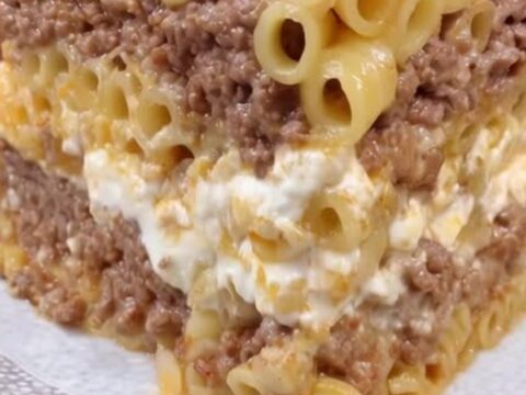 A tall, perfectly layered slice of Greek pastitsio on a white plate with visible pasta and meat.