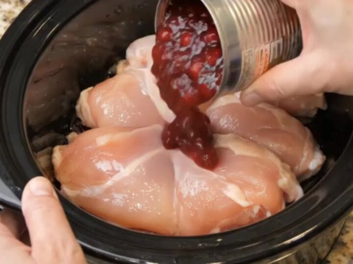 Tender shredded chicken coated in a glossy, ruby-red cranberry sauce inside a slow cooker.