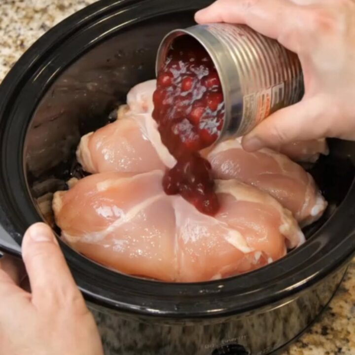 Tender shredded chicken coated in a glossy, ruby-red cranberry sauce inside a slow cooker.