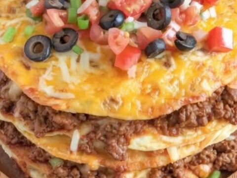 A close-up of a triple-layer Mexican pizza on a wooden platter with melted cheese, tomatoes, and sour cream.