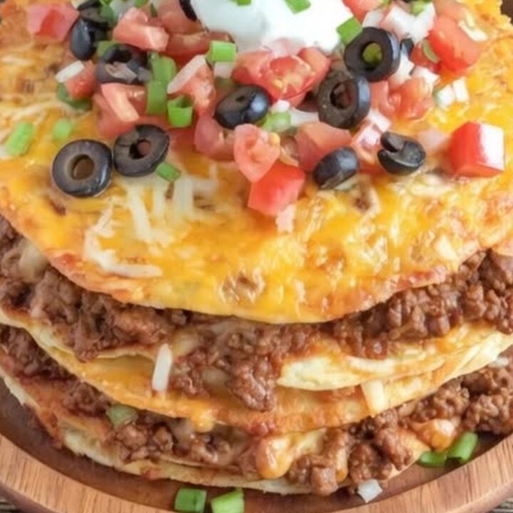 A close-up of a triple-layer Mexican pizza on a wooden platter with melted cheese, tomatoes, and sour cream.