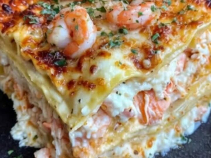 A thick, steaming slice of seafood lasagna served on a dark ceramic plate with visible shrimp and crab.