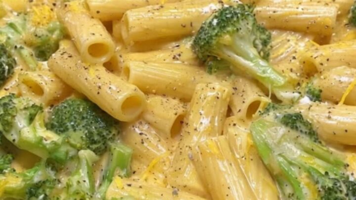 A close-up of creamy rigatoni pasta mixed with bright green broccoli florets in a black skillet.