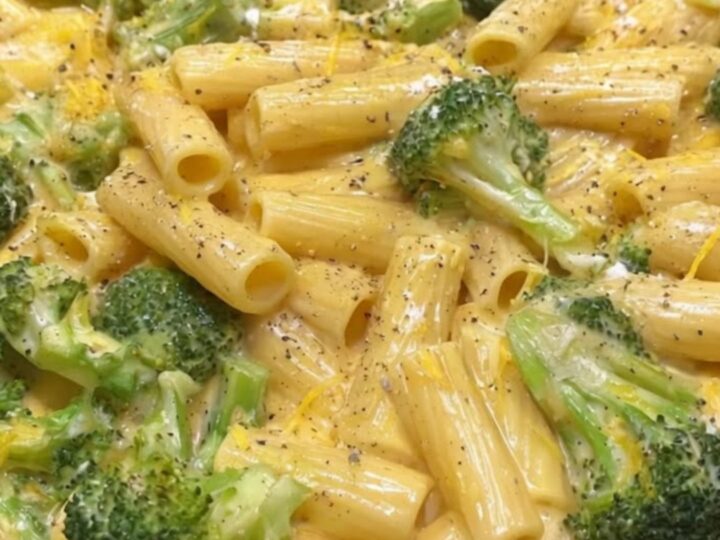 A close-up of creamy rigatoni pasta mixed with bright green broccoli florets in a black skillet.