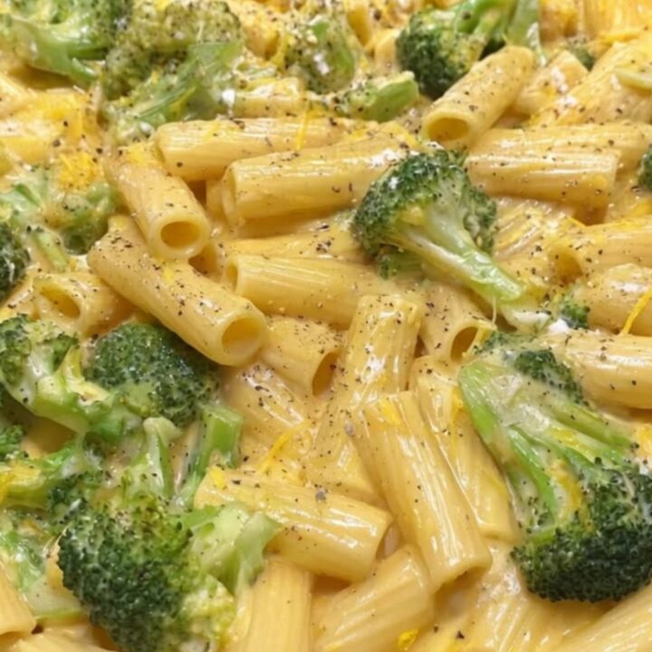 A close-up of creamy rigatoni pasta mixed with bright green broccoli florets in a black skillet.
