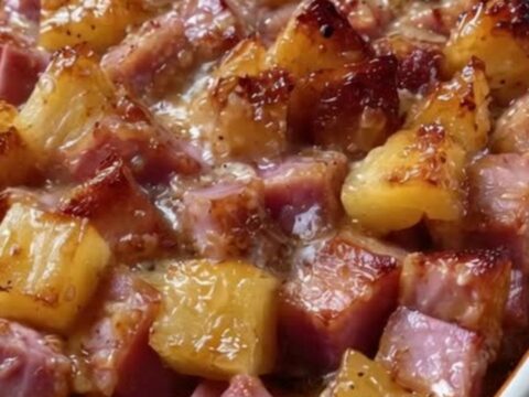 A close-up of a white ceramic dish filled with diced ham and caramelized pineapple chunks with a glossy brown sugar glaze.