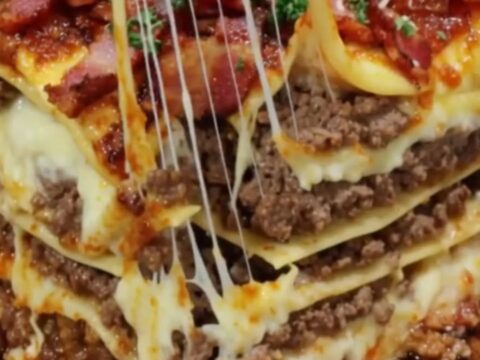 A tall, decadent slice of bacon cheeseburger lasagna showing layers of beef and melted cheese.