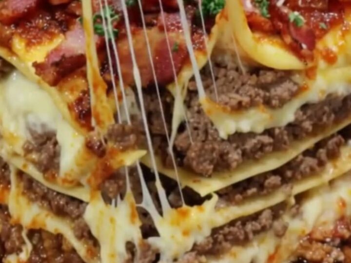 A tall, decadent slice of bacon cheeseburger lasagna showing layers of beef and melted cheese.