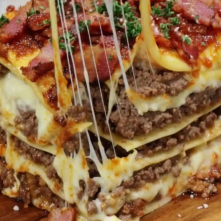 A tall, decadent slice of bacon cheeseburger lasagna showing layers of beef and melted cheese.