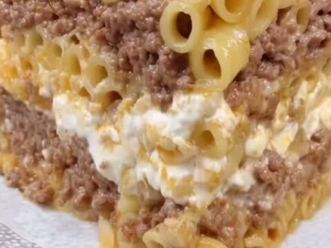 A thick square of baked pastitsio showing distinct layers of pasta and spiced meat with a browned crust.