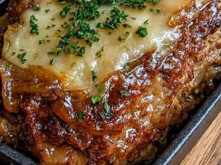 A freshly baked French onion meatloaf in a cast-iron dish with melted Gruyère cheese.