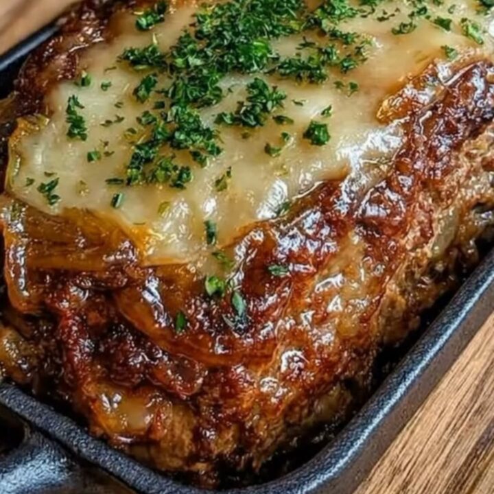 A freshly baked French onion meatloaf in a cast-iron dish with melted Gruyère cheese.