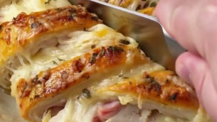 A golden, flaky crescent braid filled with chicken, ham, and melted Swiss cheese on a baking sheet.