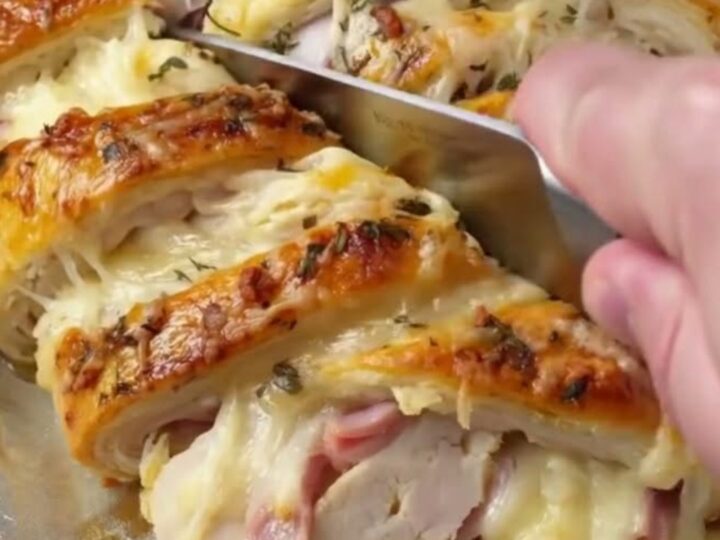 A golden, flaky crescent braid filled with chicken, ham, and melted Swiss cheese on a baking sheet.