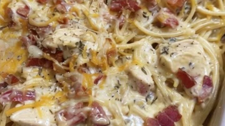 A creamy chicken spaghetti bake in a white rectangular dish, topped with melted cheese and bacon.