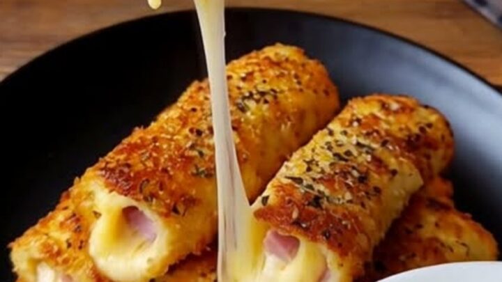 A plate of golden, crispy baked ham and mozzarella egg rolls sitting on a wooden counter.