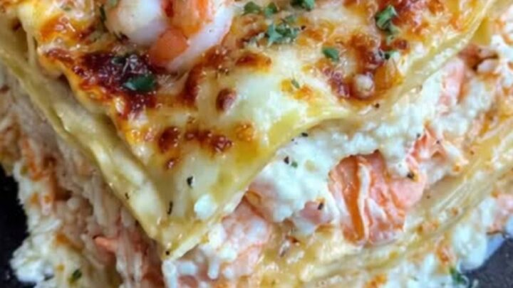 A slice of creamy seafood lasagna on a plate showing layers of shrimp, crab, and cheese.