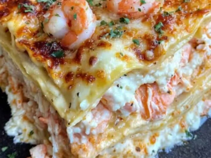 A slice of creamy seafood lasagna on a plate showing layers of shrimp, crab, and cheese.