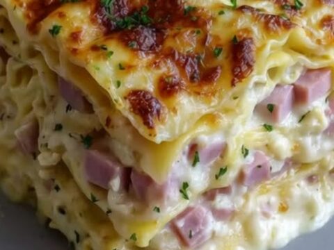 A steaming slice of creamy ham and cheese lasagna on a white plate with visible layers.