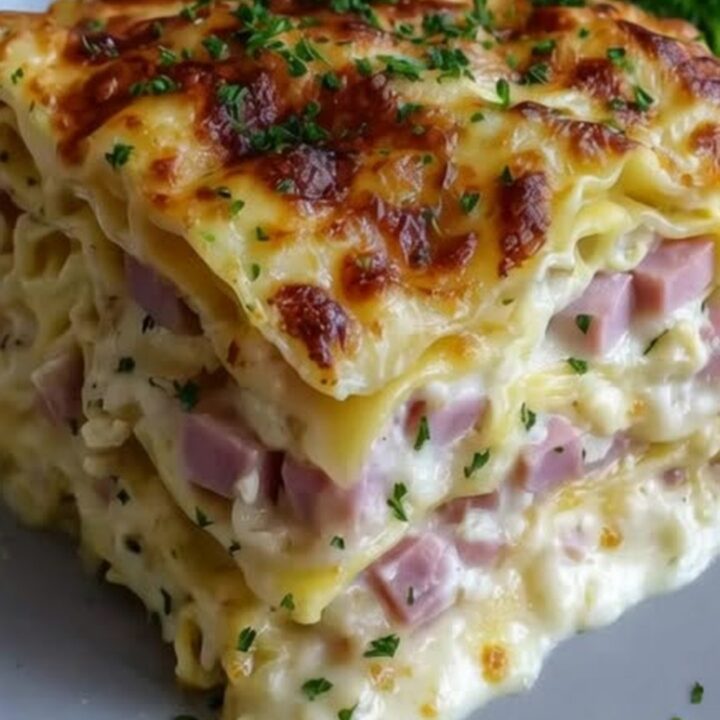 A steaming slice of creamy ham and cheese lasagna on a white plate with visible layers.