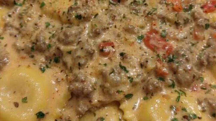 A close-up of a serving spoon lifting creamy Cajun sausage ravioli from a wide skillet with steam rising.