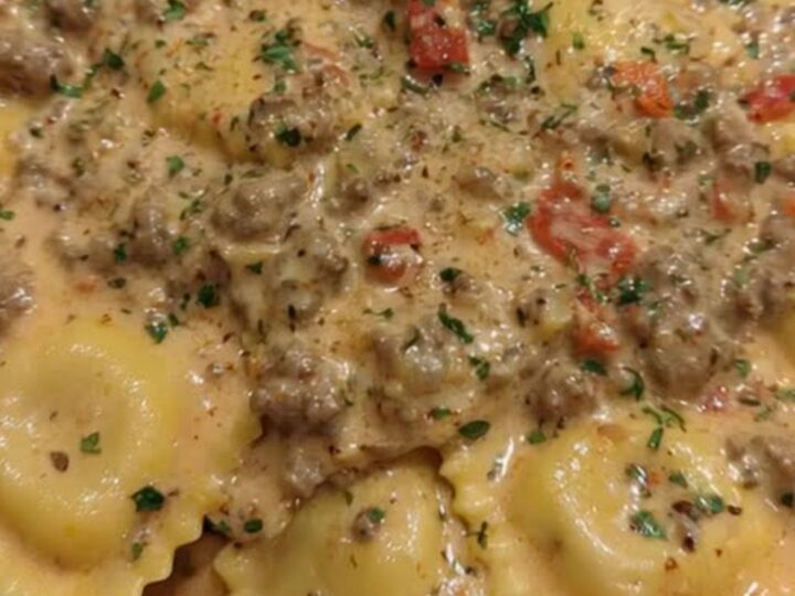A close-up of a serving spoon lifting creamy Cajun sausage ravioli from a wide skillet with steam rising.