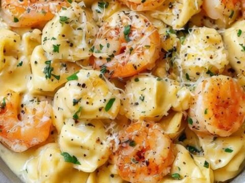 A close-up of a creamy shrimp and tortellini dish in a grey bowl, steaming and ready to eat.
