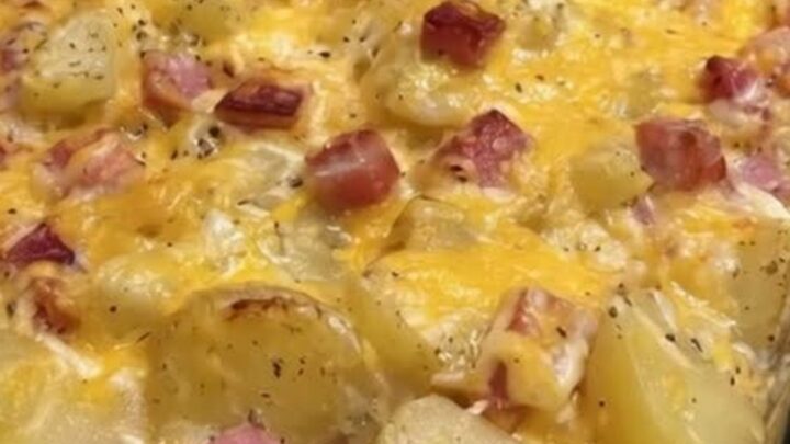A bubbling, golden-brown cheesy ham and potato casserole in a glass dish.