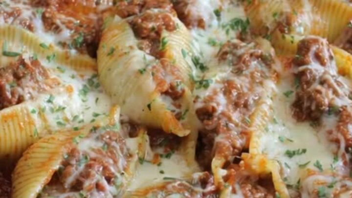 A cast-iron skillet filled with jumbo pasta shells stuffed with ground beef and topped with melted mozzarella.