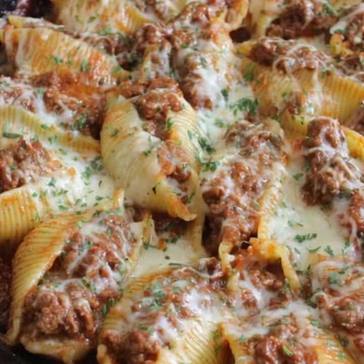 A cast-iron skillet filled with jumbo pasta shells stuffed with ground beef and topped with melted mozzarella.