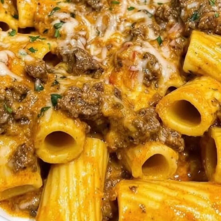 A white serving dish filled with creamy garlic butter beef rigatoni topped with fresh parsley and melted parmesan cheese.