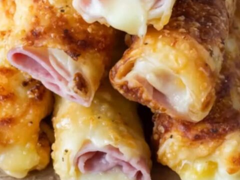 A plate of crispy golden baked ham and cheese roll-ups sitting on a white plate in a bright kitchen.