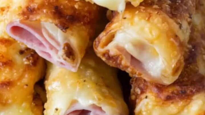 A plate of crispy golden baked ham and cheese roll-ups sitting on a white plate in a bright kitchen.