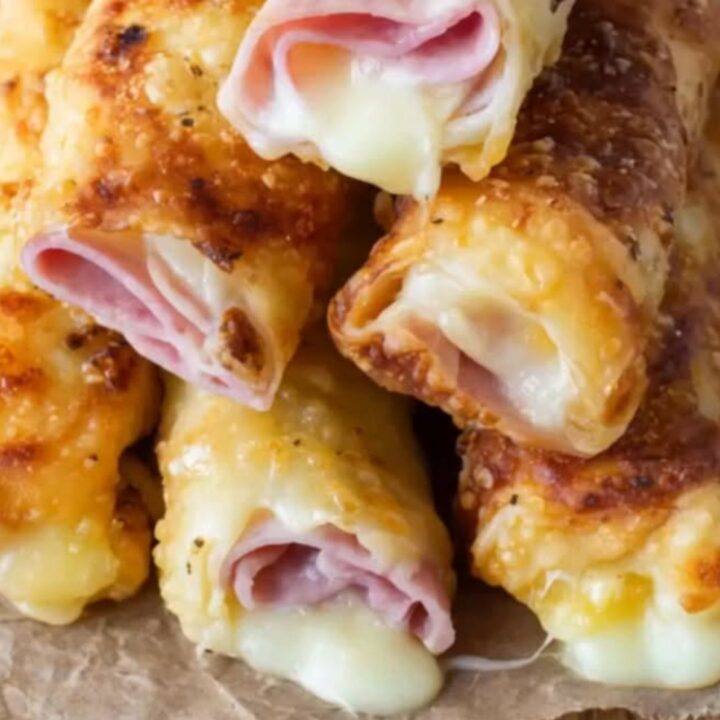 A plate of crispy golden baked ham and cheese roll-ups sitting on a white plate in a bright kitchen.