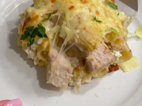 A bubbly, golden-brown chicken Alfredo lasagna in a glass baking dish with a cheese pull.