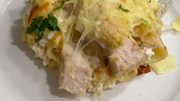A bubbly, golden-brown chicken Alfredo lasagna in a glass baking dish with a cheese pull.
