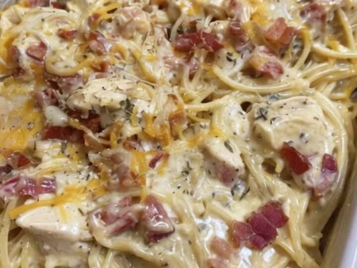 A golden, bubbling chicken spaghetti bake in a white dish with crispy bacon bits on top.