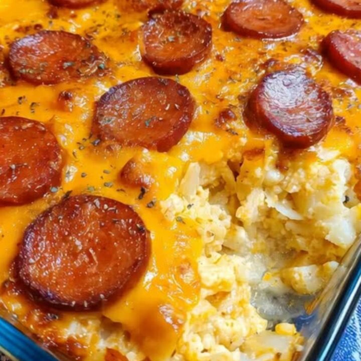 A warm, cheesy smoked sausage and potato casserole in a glass baking dish, with steam rising from a freshly served portion.