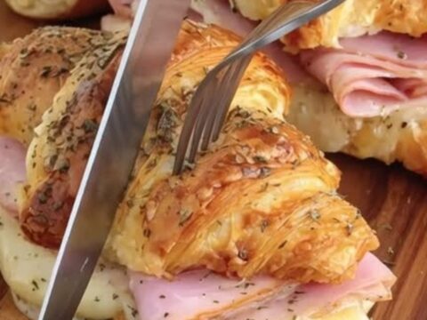 Golden, buttery croissants filled with warm ham and melted Swiss cheese on a wooden board.