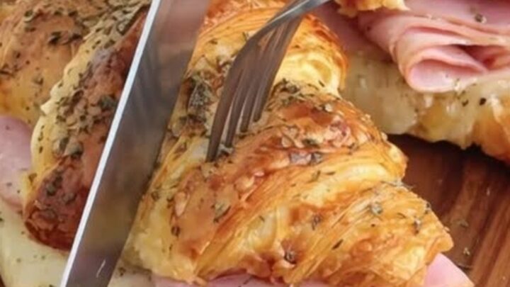 Golden, buttery croissants filled with warm ham and melted Swiss cheese on a wooden board.