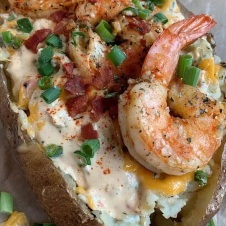 A freshly baked potato overflowing with creamy sauce, melted cheddar, crispy bacon, and seared cajun shrimp.