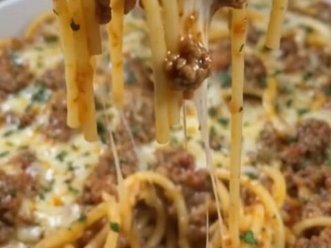 A steaming baking dish filled with Cajun beef spaghetti topped with a thick, golden layer of melted cheddar cheese.
