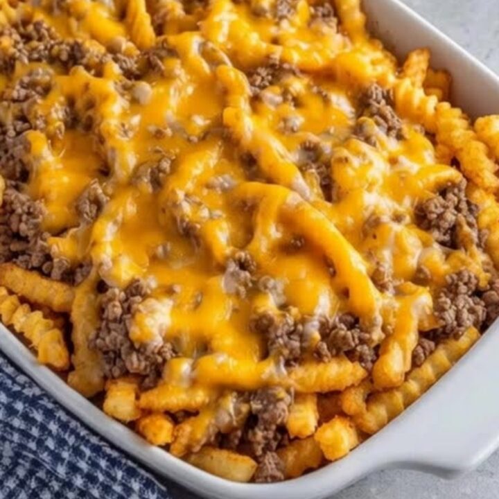 A white baking dish filled with a cheesy ground beef and french fry casserole.