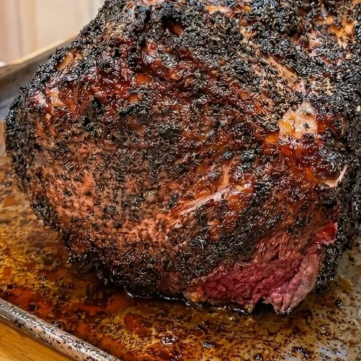 A beautifully roasted prime rib with a fresh herb crust sitting on a white plate.