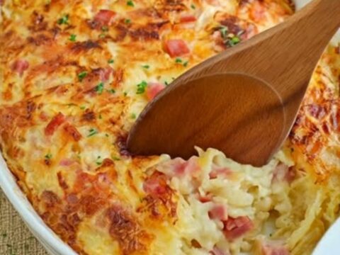 A golden-baked ham and cheese hash brown casserole in an oval dish with steam rising.
