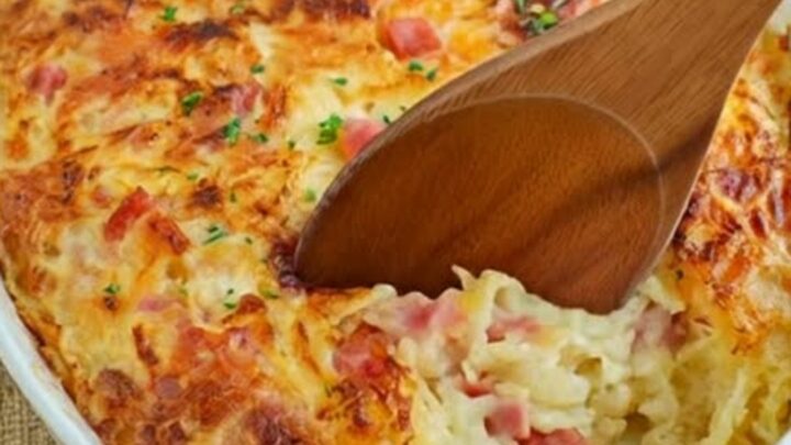A golden-baked ham and cheese hash brown casserole in an oval dish with steam rising.