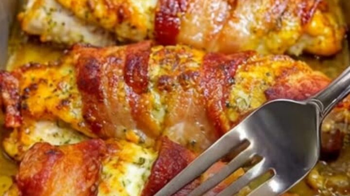 A golden, bacon-wrapped chicken breast resting in a metal baking pan with a crispy, savory crust.