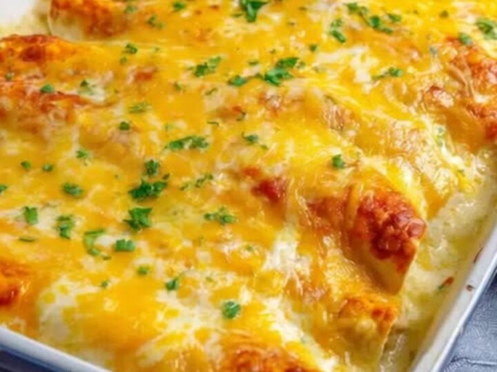 A blue ceramic baking dish filled with golden, bubbling sour cream chicken enchiladas garnished with fresh green parsley.