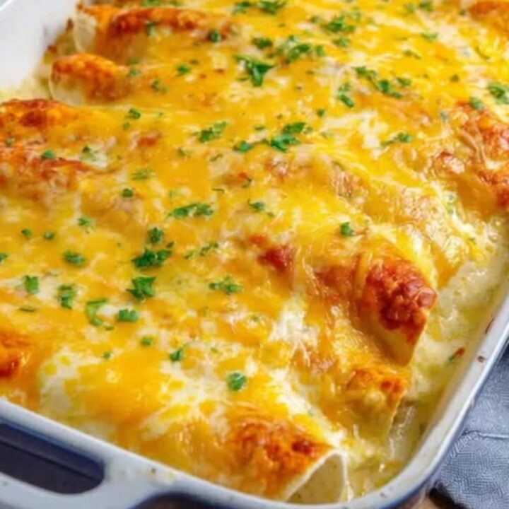 A blue ceramic baking dish filled with golden, bubbling sour cream chicken enchiladas garnished with fresh green parsley.